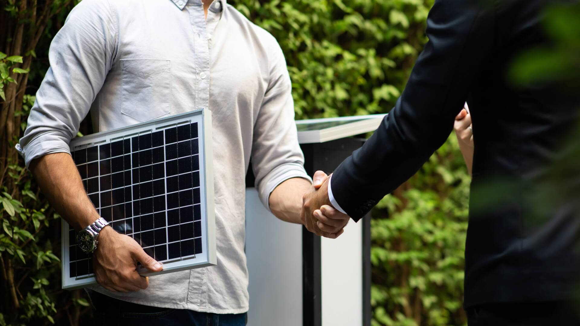 two men hand shaking and one holding solar panel